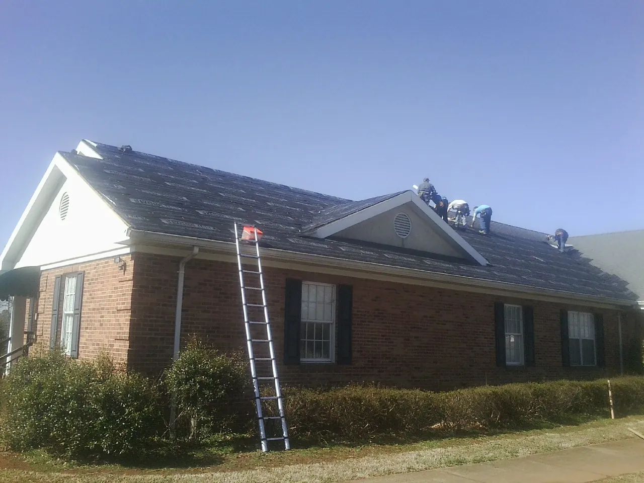 Crew tearing shingles off a brick ranch roof with a ladder set — Metal Roof Repair work by our crew in Cherryville