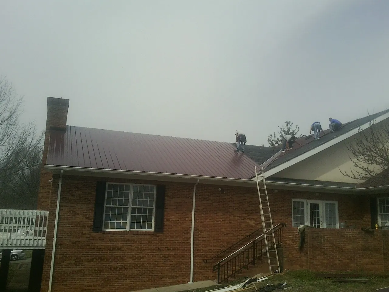 Crew setting red metal roofing panels on a brick home in Cherryville