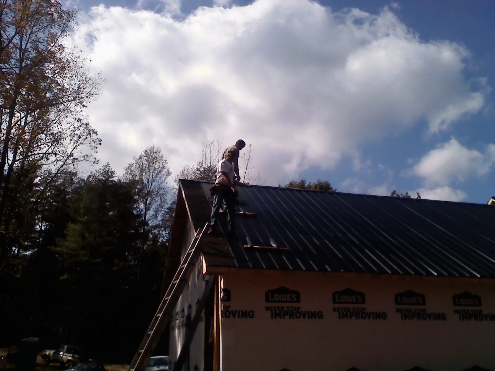 Roofer fastening dark metal panels high against a cloudy sky, from a Roof Inspection job in Cherryville